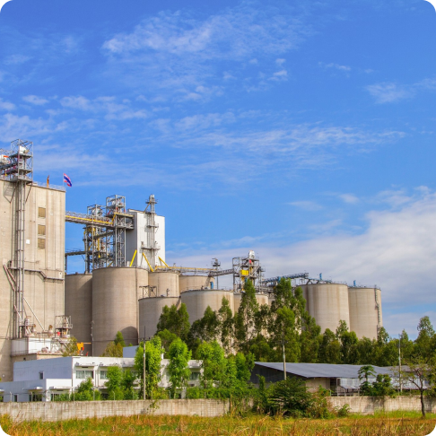 Cement grinding plant with blue processing towers, white storage silos, and large pipeline system under blue sky.